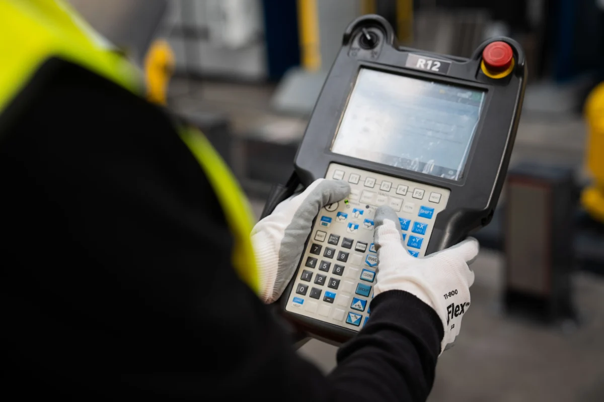 Operator obsługuje panel sterowania robotem przemysłowym w zautomatyzowanej produkcji