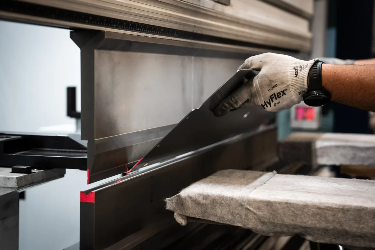 Operator w rękawicach umieszcza arkusz blachy w matrycy prasy krawędziowej