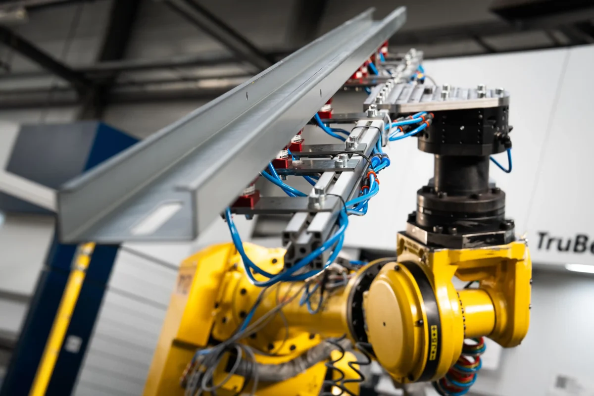 Robot przemysłowy trzymający długi profil blachy podczas procesu gięcia na prasie krawędziowej